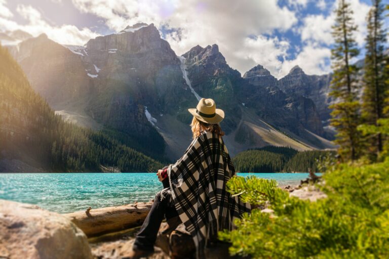 a woman sits on a rock beside the lake